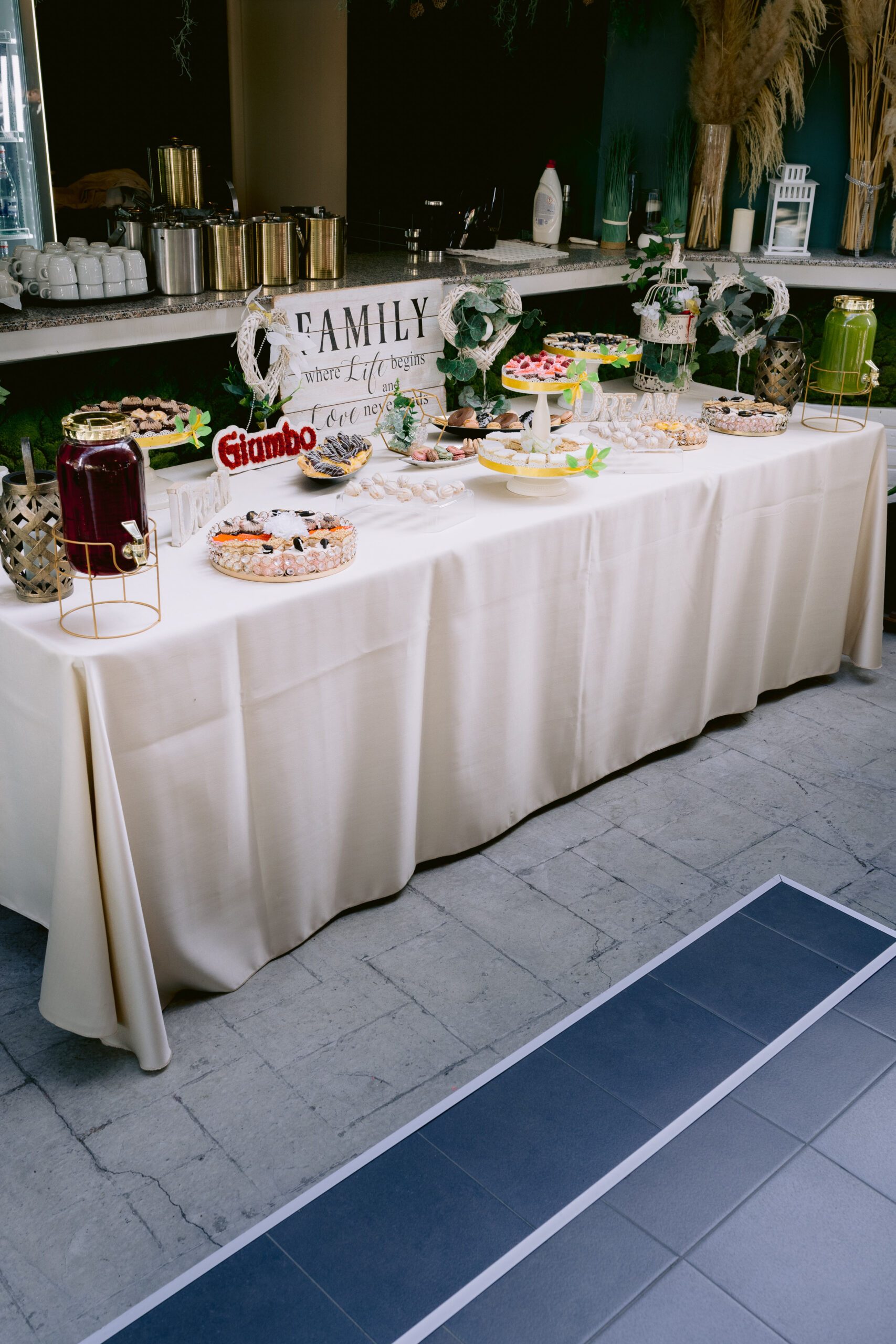 Masă dulce de eveniment pregătită de Cofetăria Giumbo, pe o masă lungă cu față albă, cu prăjituri și decor discret