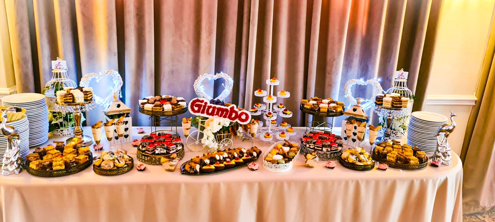 Masă dulce de eveniment pregătită de Cofetăria Giumbo, în tonuri calde, cu prăjituri asortate pe platouri